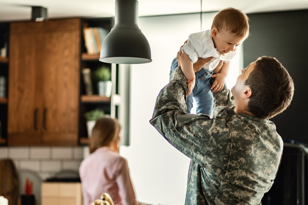 Military man holding son wife in background